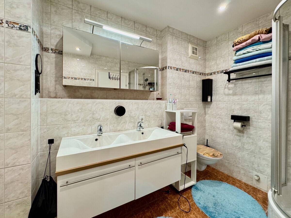 Helles Badezimmer mit Doppelwaschbecken, Toilette, Duschkabine und Spiegelschrank.