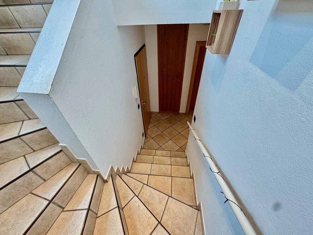 Geflieste Treppe mit Holzgeländer, die zu den unteren Etagen führt.