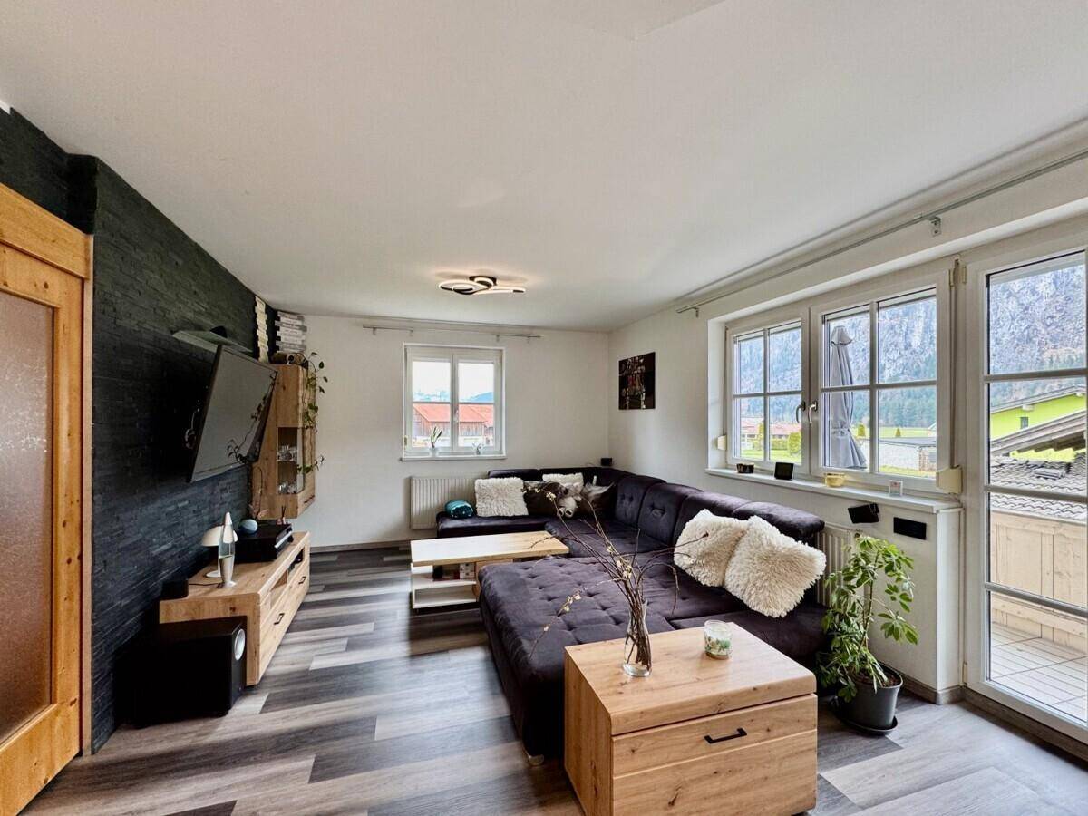 Heller Wohnbereich mit großem Sofa, Steinwand und Zugang zu einem sonnigen Balkon.