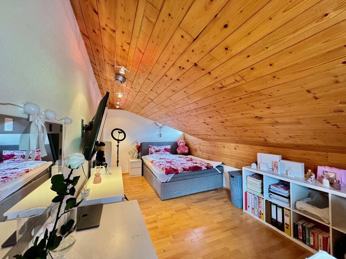 Gemütliches Schlafzimmer im Dachgeschoss mit Holzbalkendecke und Stauraum.