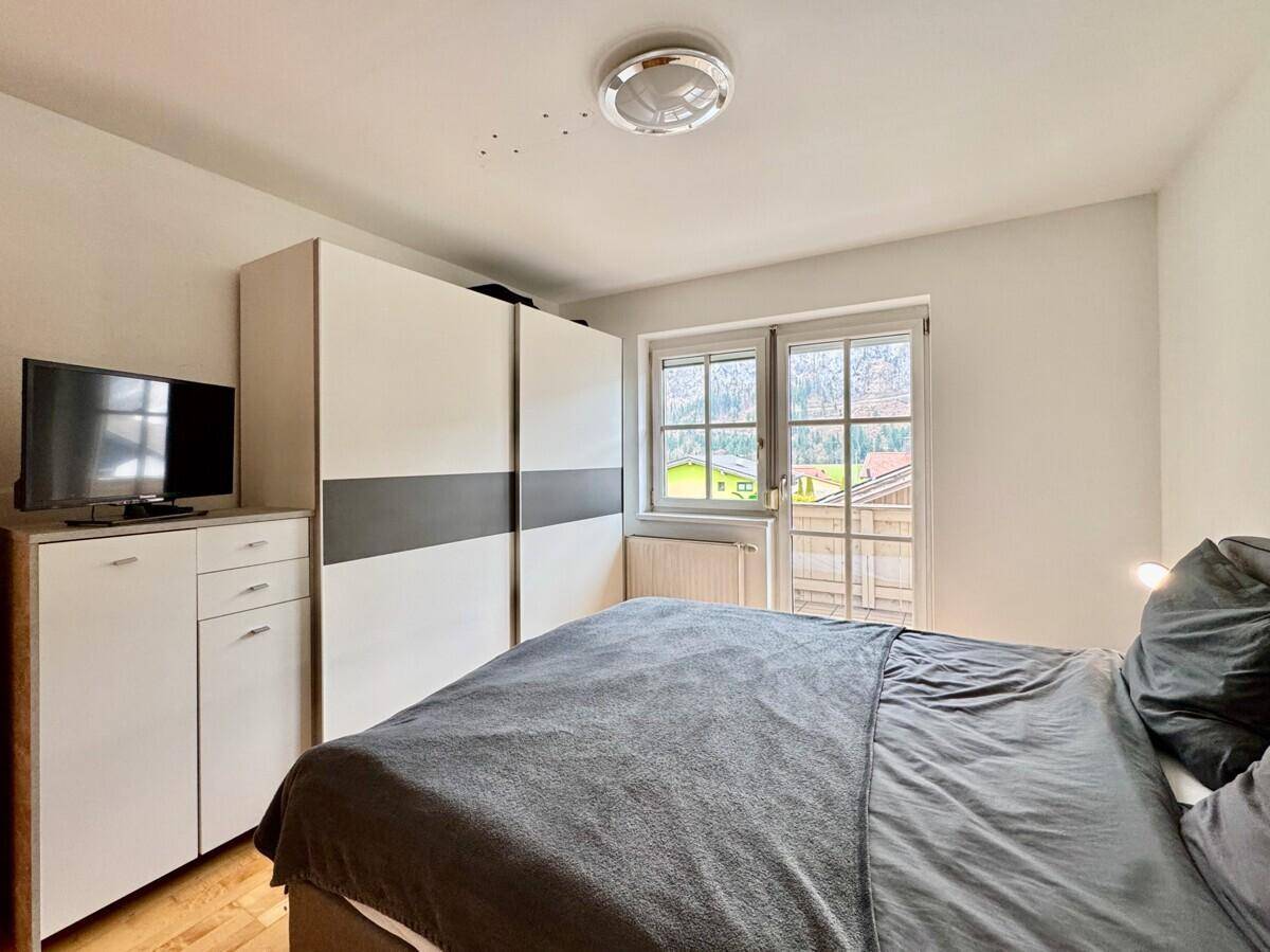 Helles Schlafzimmer mit Doppelbett, modernem Kleiderschrank und Fenster mit Bergblick.