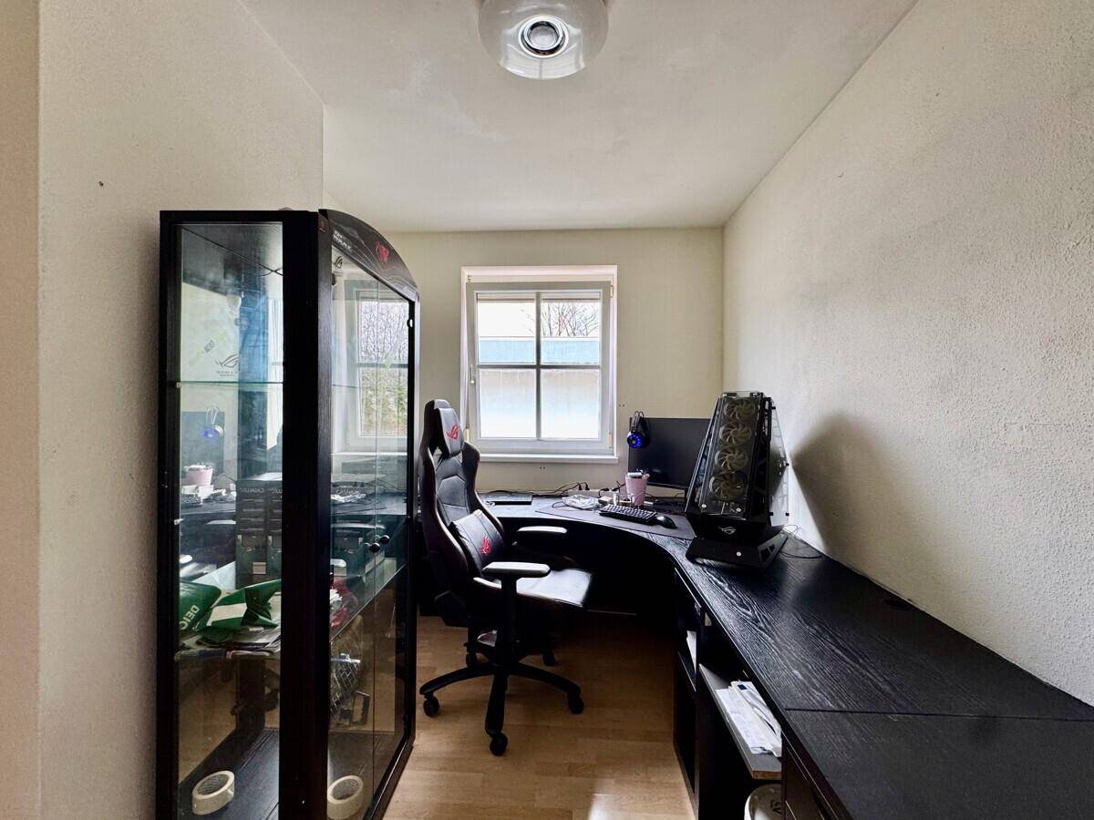 Funktionales Büro mit großem Schreibtisch, Gaming-Stuhl und Vitrine.