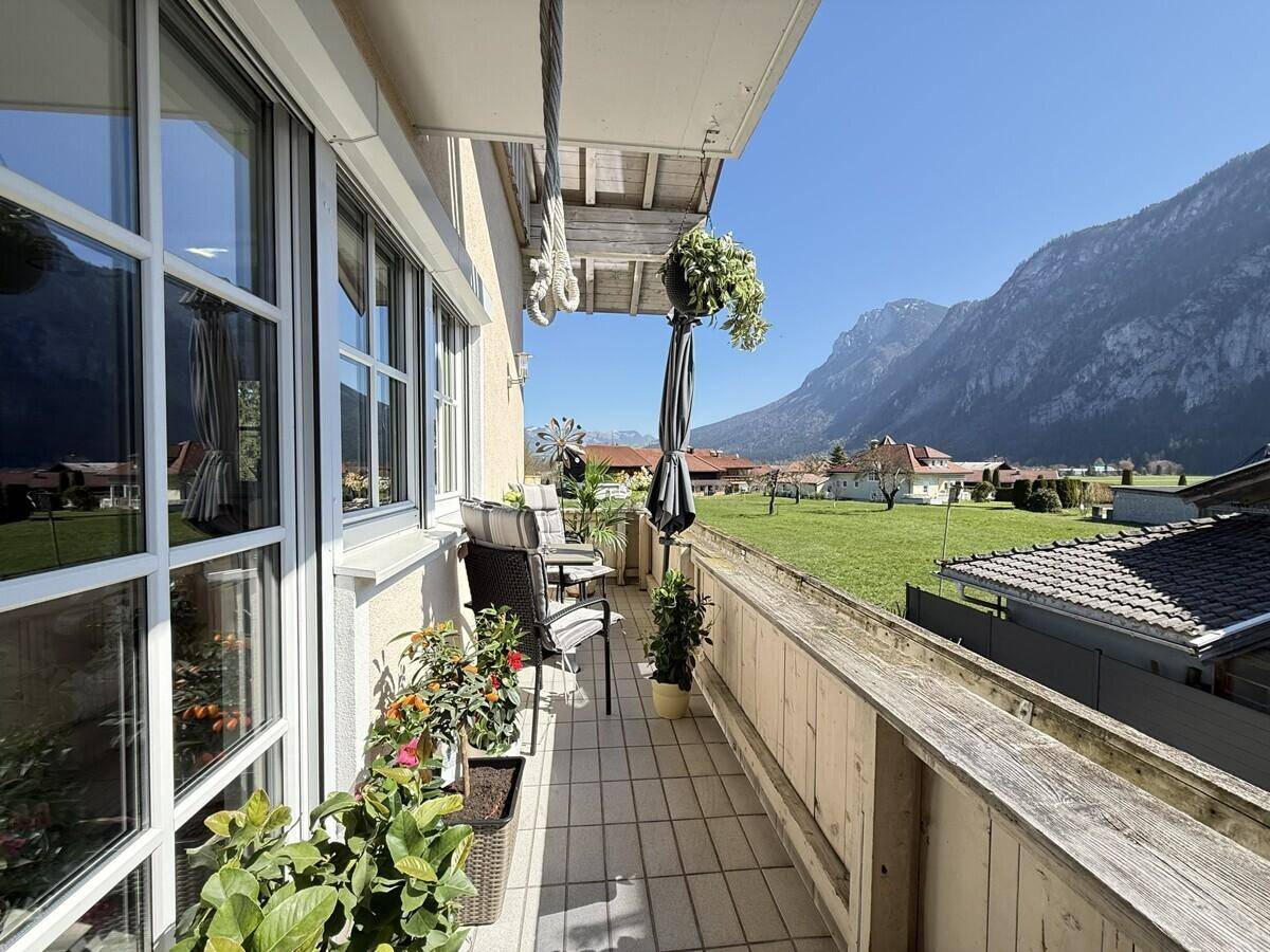 Sonniger Balkon mit Sitzgelegenheiten, Pflanzen und weitem Blick auf die Berge und Wiesen.