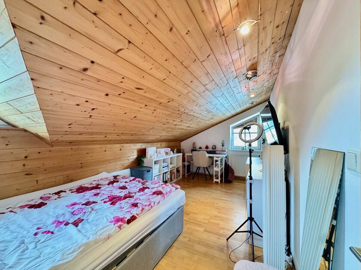 Helles Schlafzimmer im Dachgeschoss mit Holzdecke, Bett und modernem Arbeitsbereich.