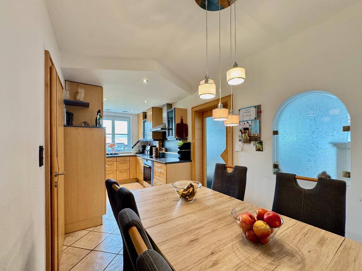 Heller Essbereich mit Holztisch und Blick in die angrenzende Küche mit Fliesenboden.
