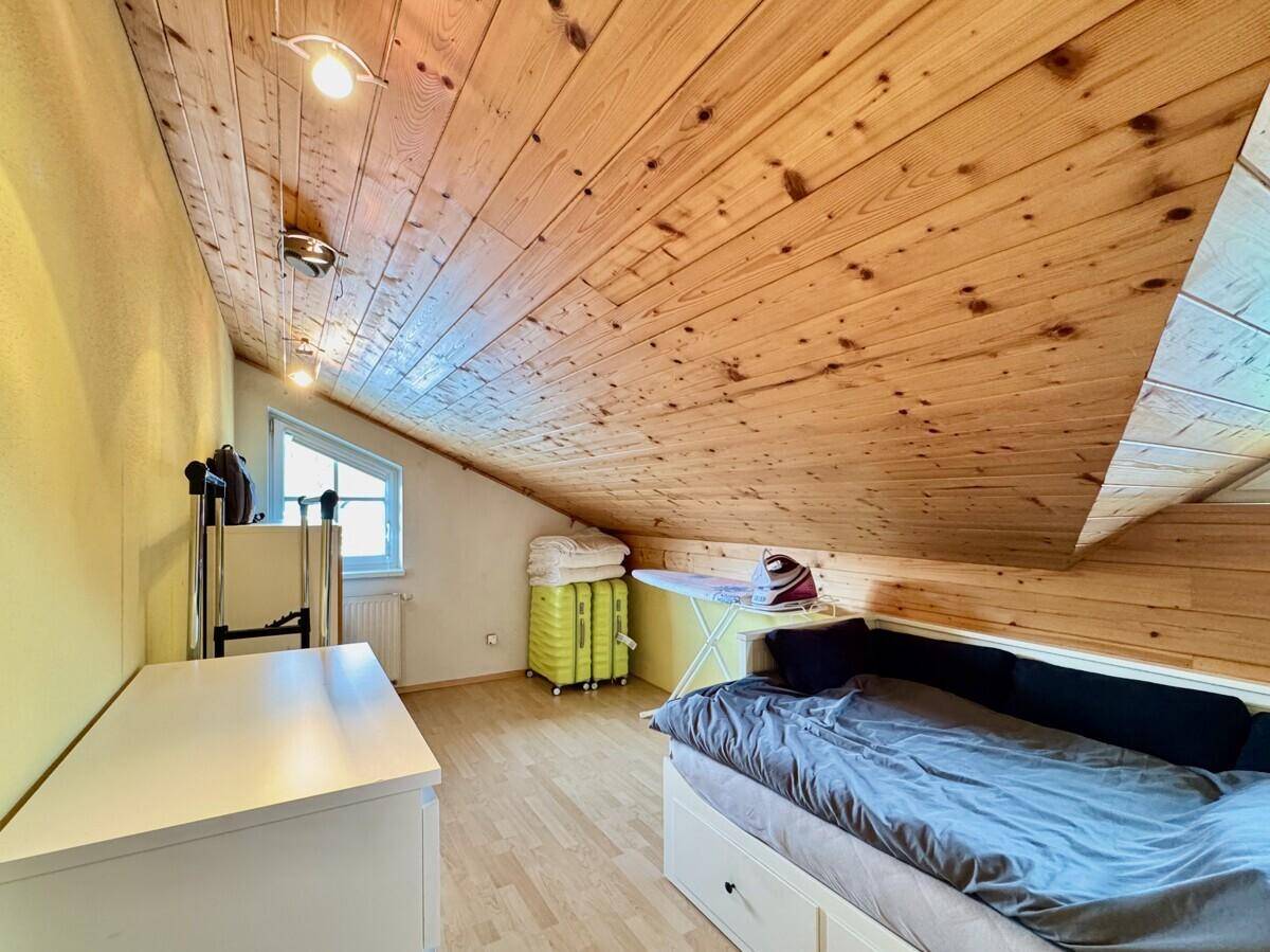 Gemütliches Dachzimmer mit Holzverkleidung, Einzelbett und kleinem Fenster.