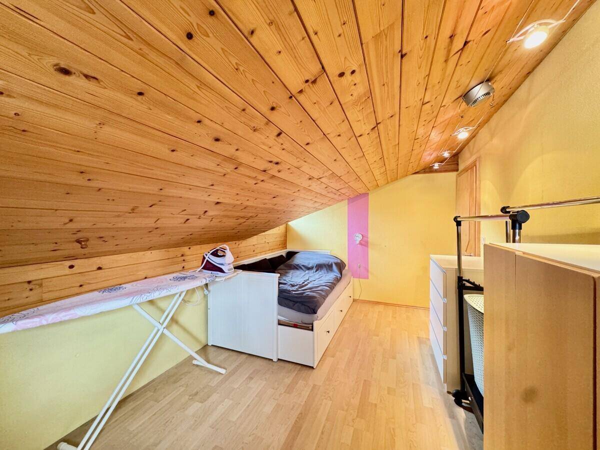 Dachzimmer mit schrägen Wänden, Holzbalkendecke und praktischer Einrichtung.