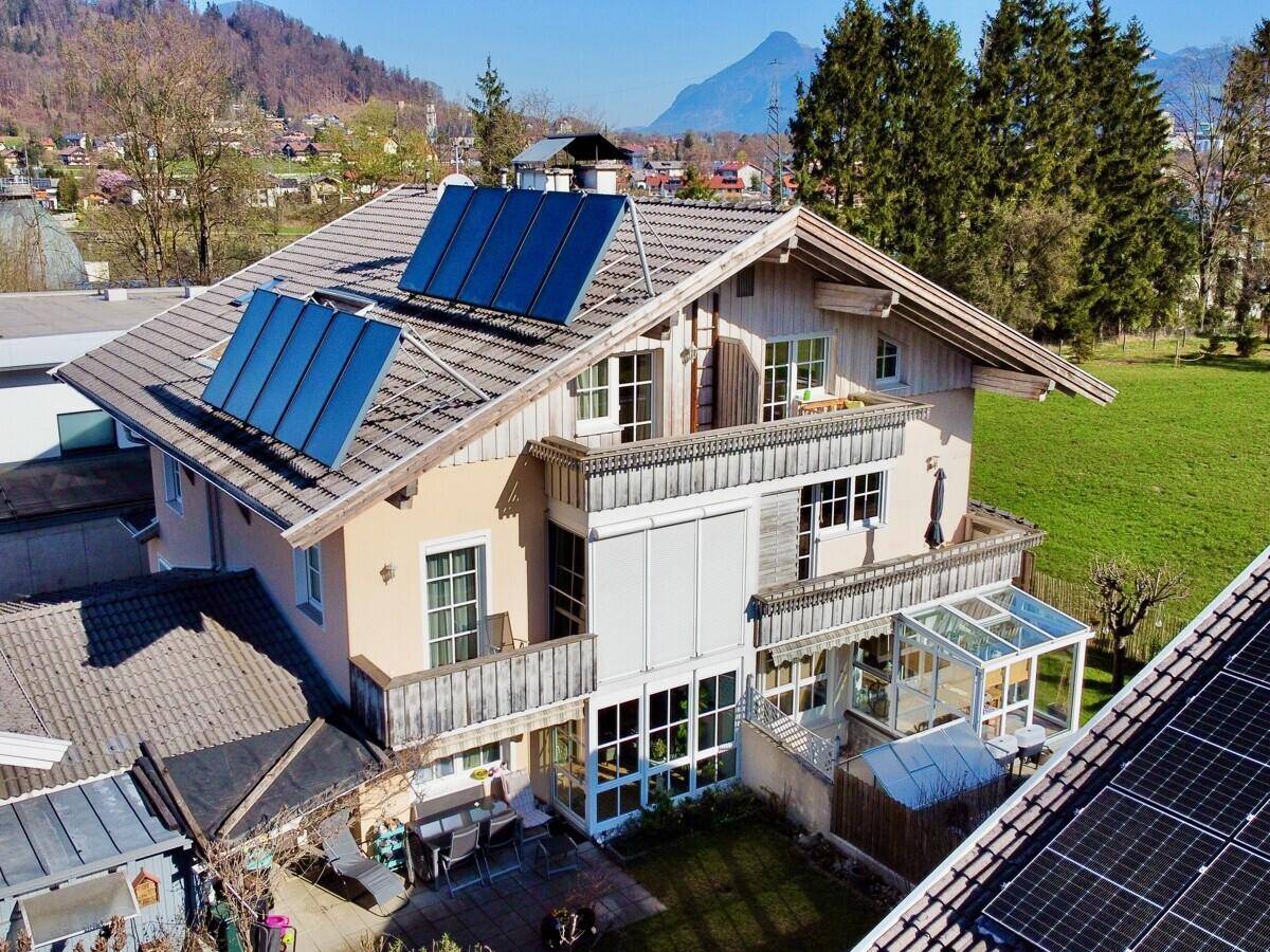 Luftaufnahme eines Hauses mit Solaranlagen, Balkonen und Bergblick.