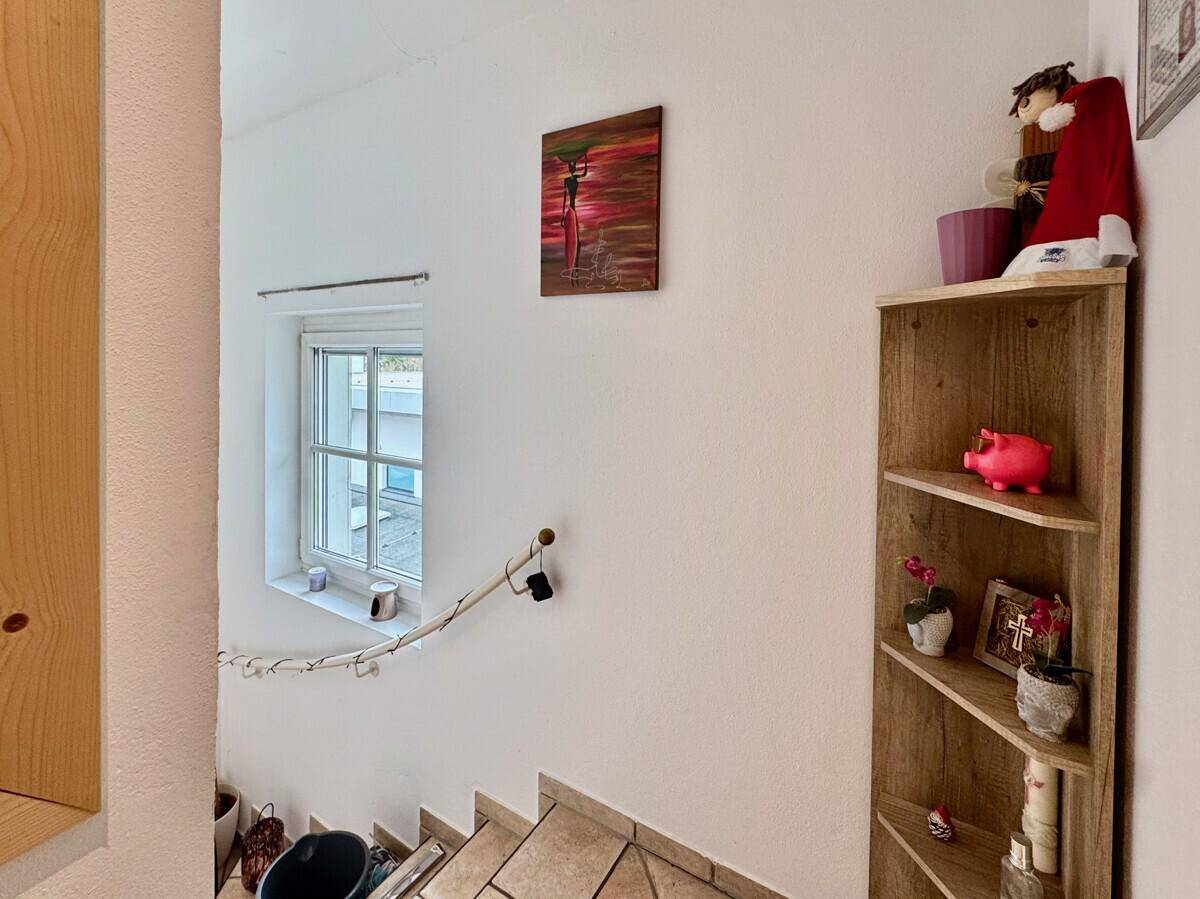 Heller Treppenaufgang mit Fenster und dekorativem Holzregal.