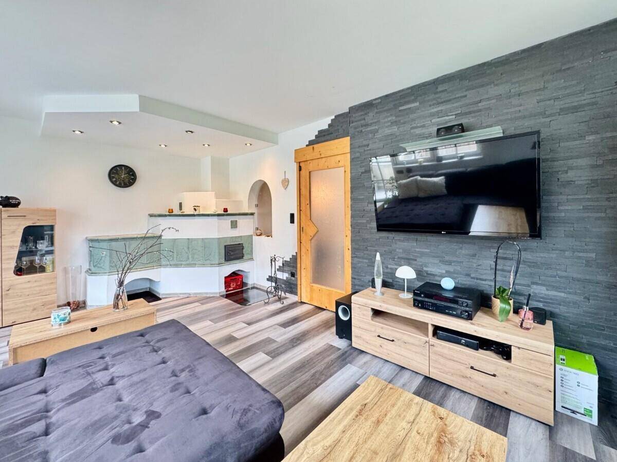 Wohnzimmer mit traditionellem Kachelofen, moderner Steinwand und Holztüren.