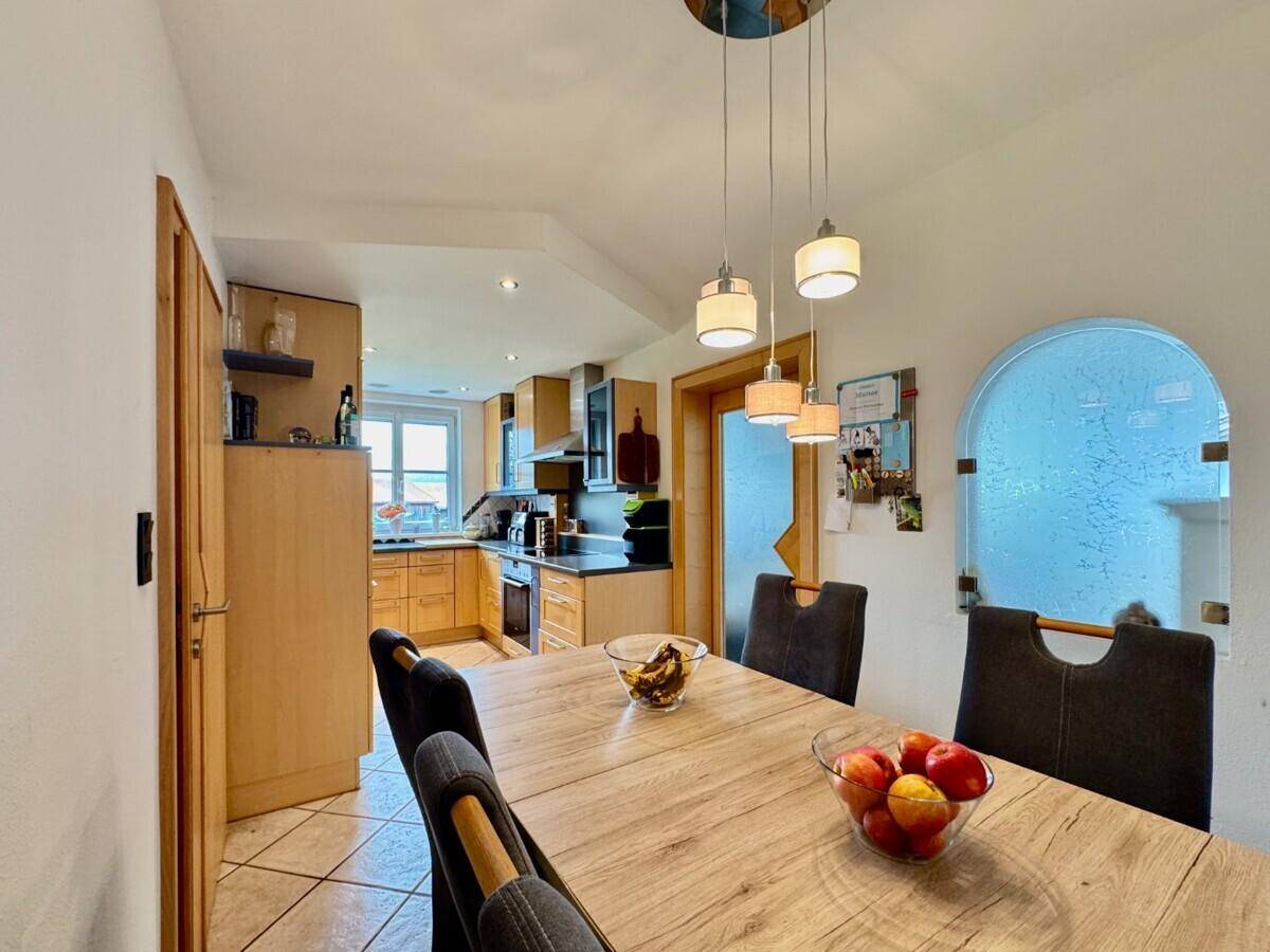Heller Essbereich mit Holztisch und Blick in die angrenzende Küche mit Fliesenboden.
