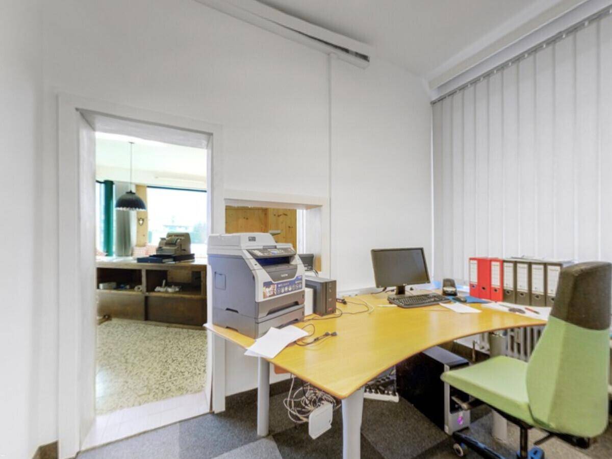 Büro mit Schreibtisch, Computer, Drucker und Blick in den angrenzenden Raum.