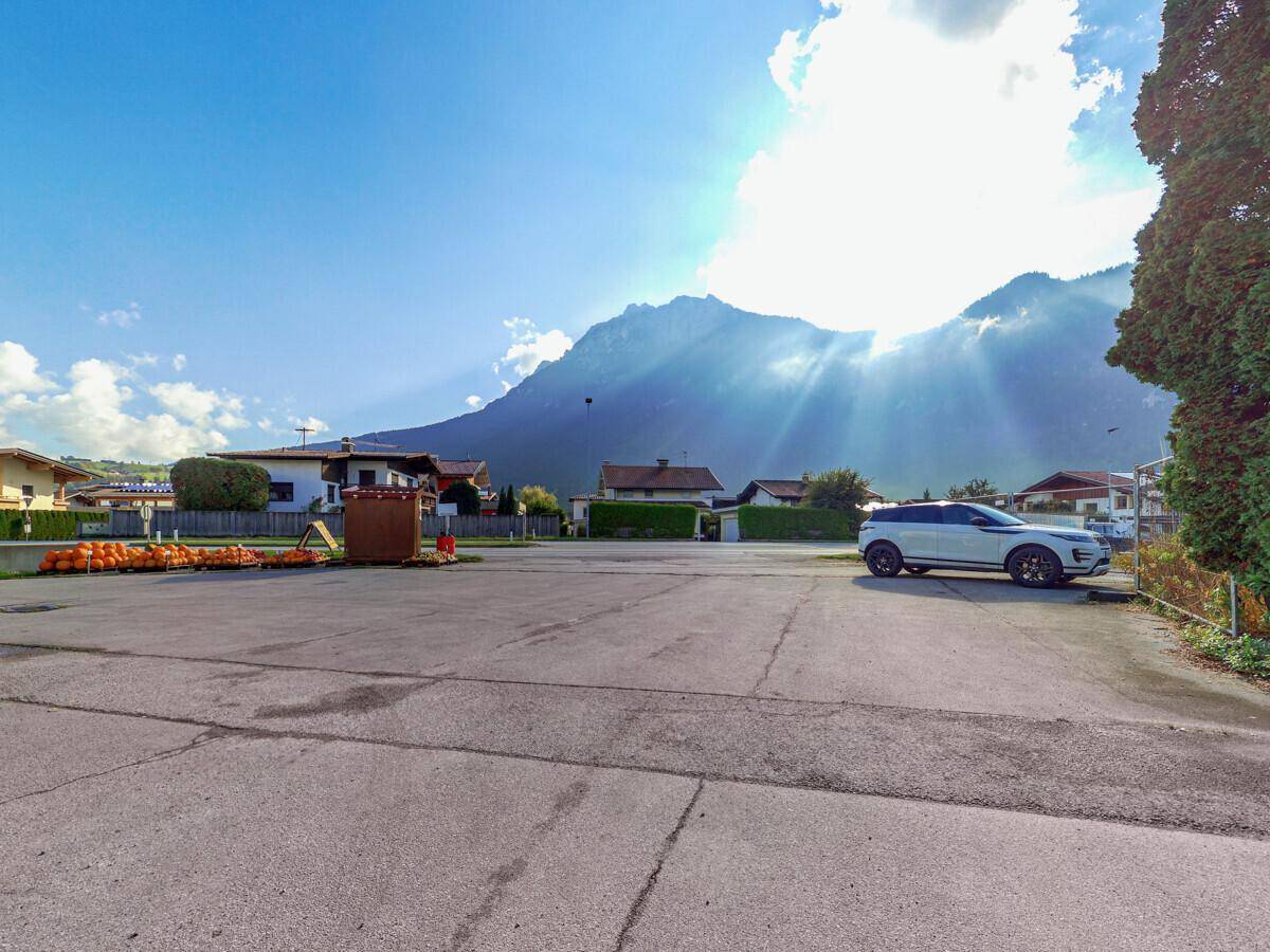 Großer asphaltierter Parkplatz vor einer Bergkulisse unter strahlend blauem Himmel.