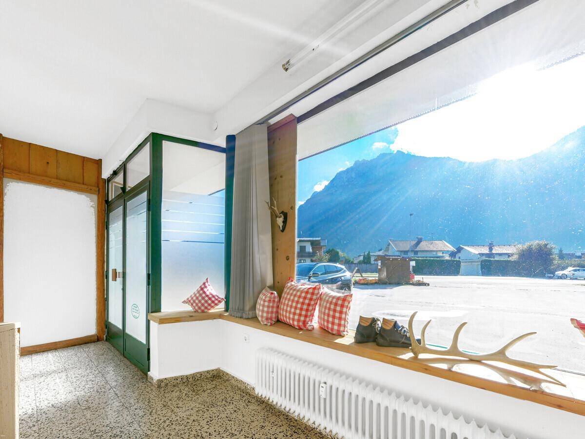 Heller Geschäftsraum mit großer Fensterfront, Fliesenboden und Bergblick.