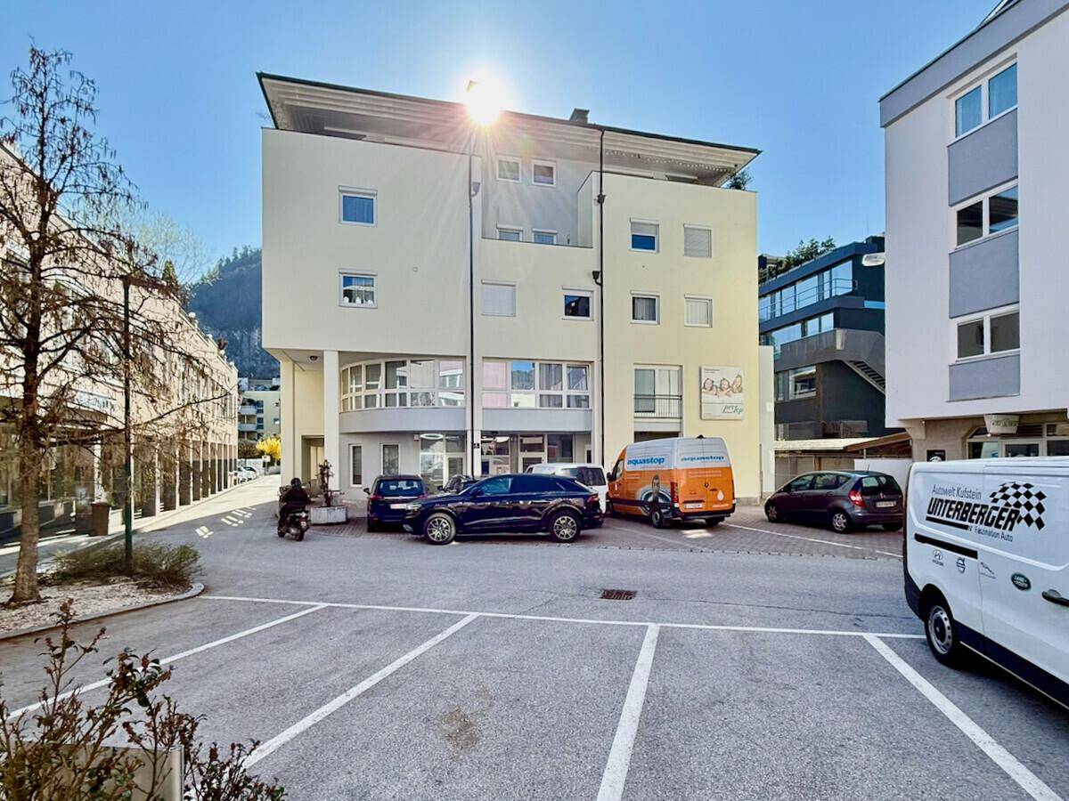 Modernes Mehrfamilienhaus mit Parkplätzen vor dem Gebäude an einem sonnigen Tag.