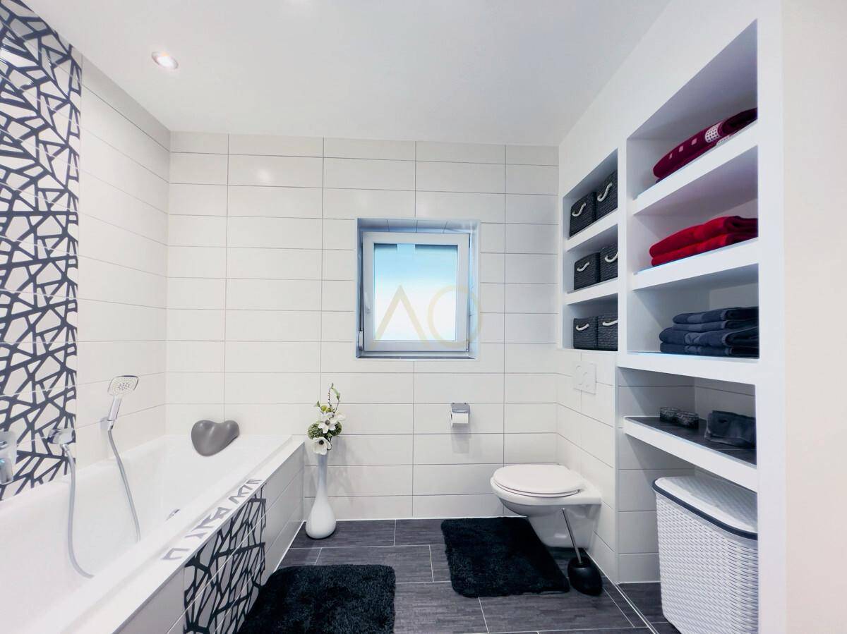 Modernes Badezimmer mit Badewanne, Wand-WC und praktischen Einbauregalen.