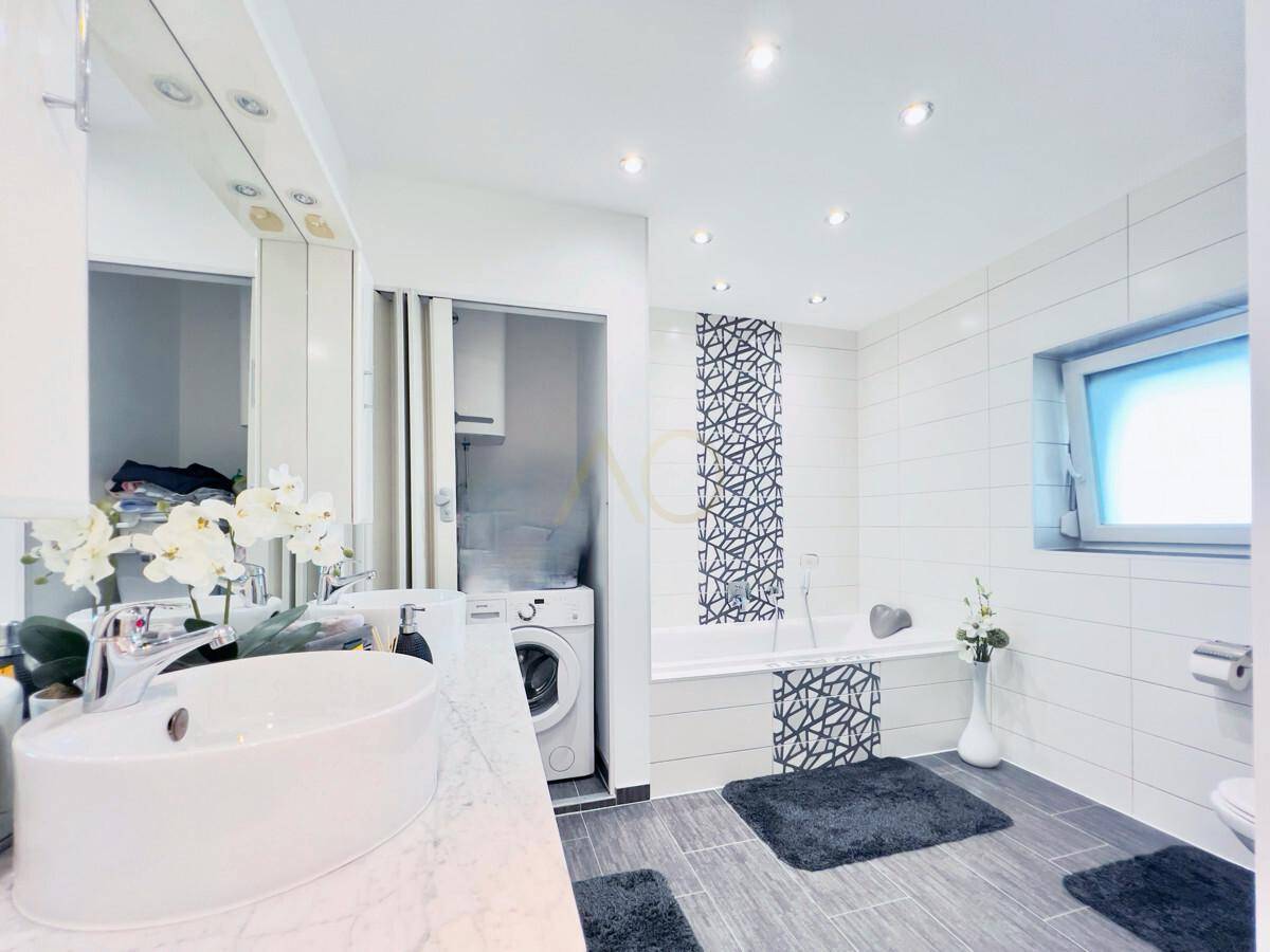 Helles Badezimmer mit Waschbecken, Badewanne und integrierter Waschmaschine.