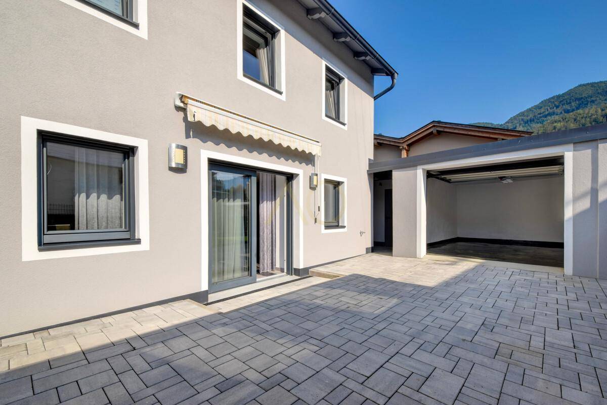 Modernes Einfamilienhaus mit Terrasse, Garage und gepflastertem Vorplatz.