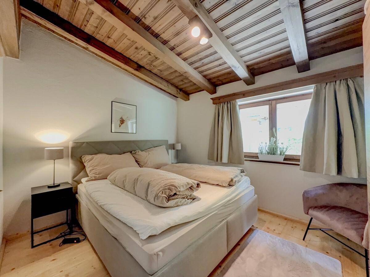 Helles Schlafzimmer mit Holzbalkendecke, Holzboden und beigem Doppelbett.