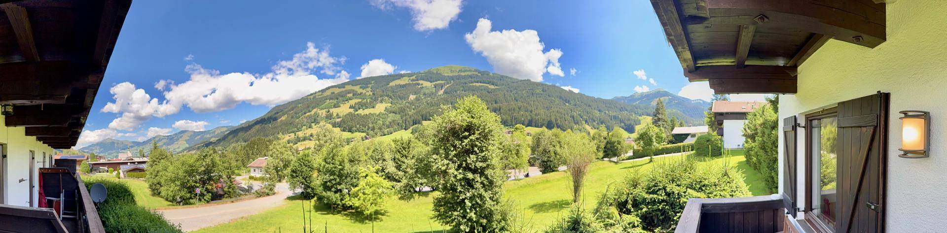 Panoramablick vom Balkon auf die weite grüne Berglandschaft unter blauem Himmel.