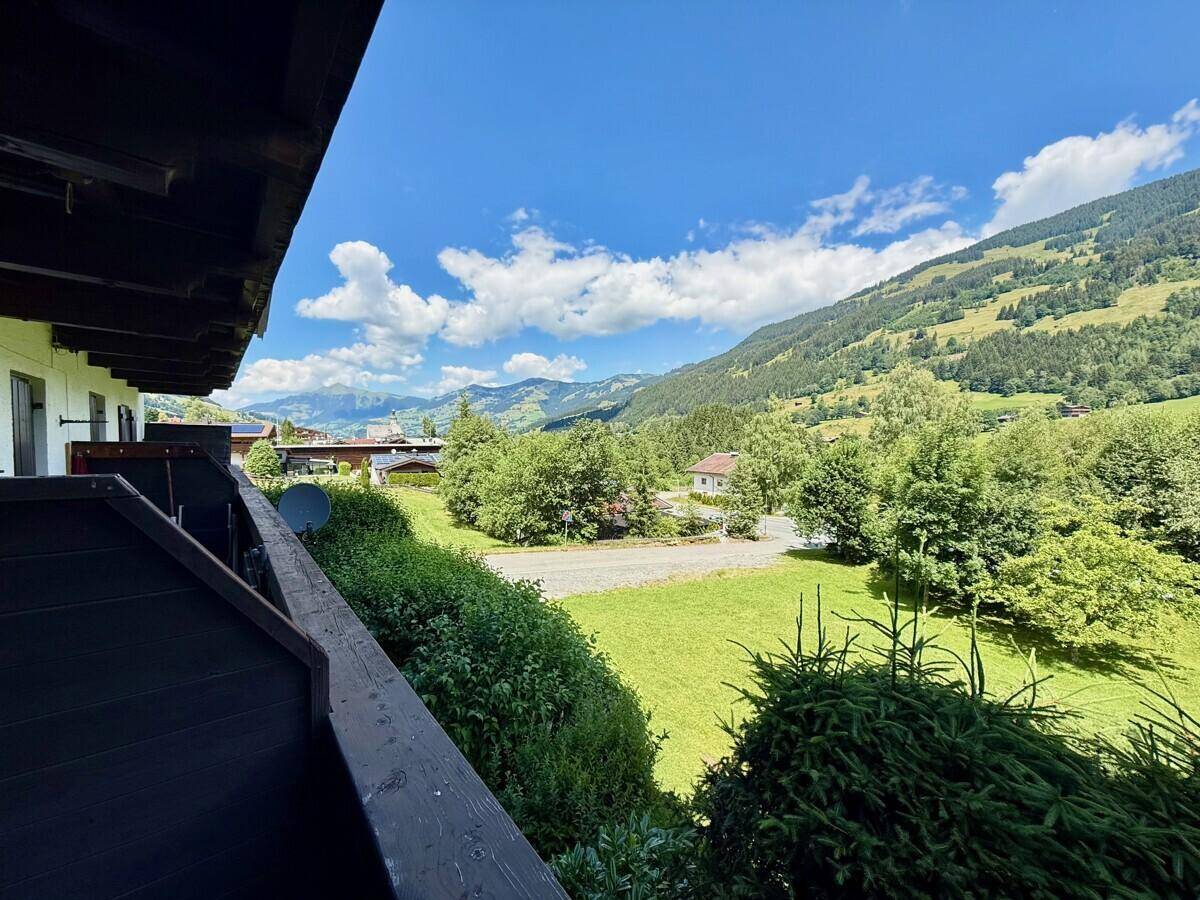 Balkon mit Blick auf die grüne Landschaft und die umliegenden Berge unter blauem Himmel.