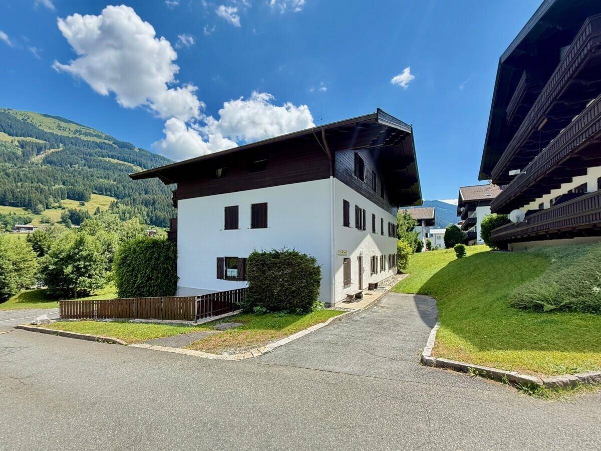 Traditionelles Gebäude mit weißer Fassade und braunen Holzelementen in einer grünen Berglandschaft.