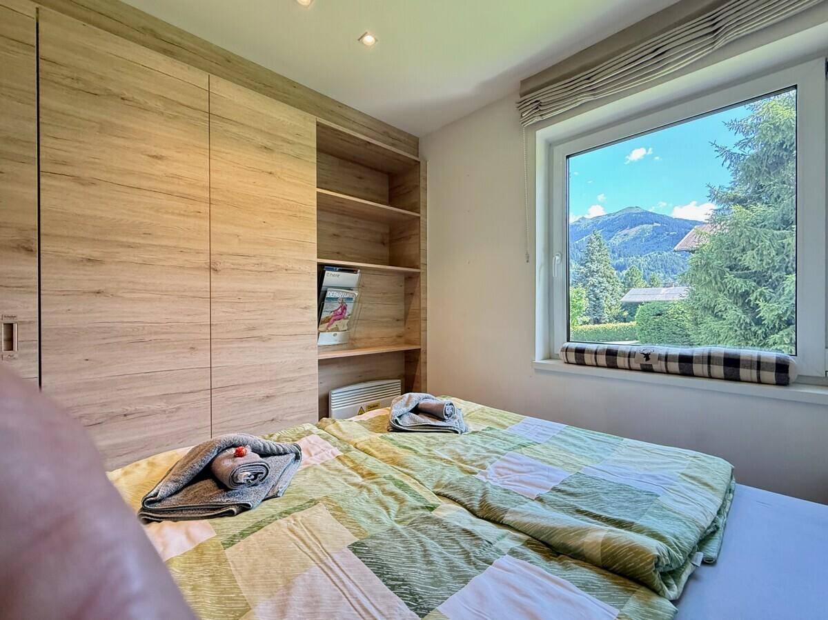 Schlafzimmer mit Doppelbett, Holzschränken und einem Fenster mit Blick auf die Berge.