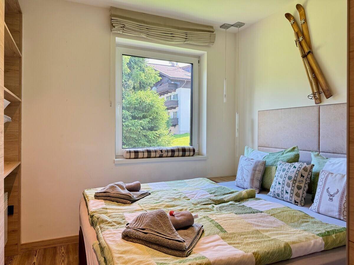 Schlafzimmer mit Doppelbett, Fenster mit Ausblick und dekorativen Skiern an der Wand.