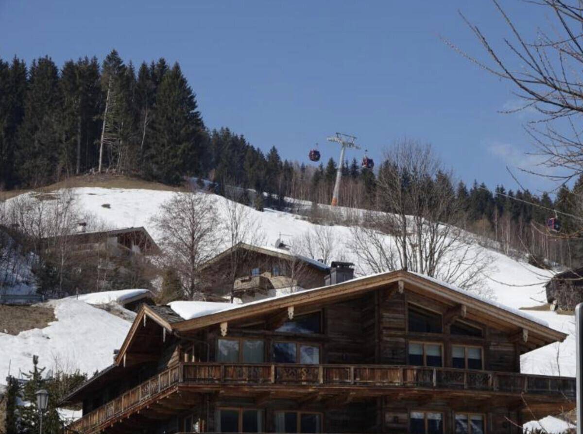 Traditionelles Holzhaus in den Bergen mit Skilift im Hintergrund und Schnee.