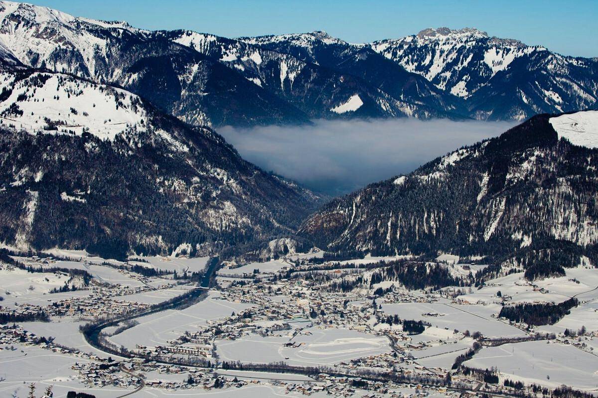 Atemberaubende Luftaufnahme eines verschneiten Tals mit einem Dorf und majestätischen Bergen.
