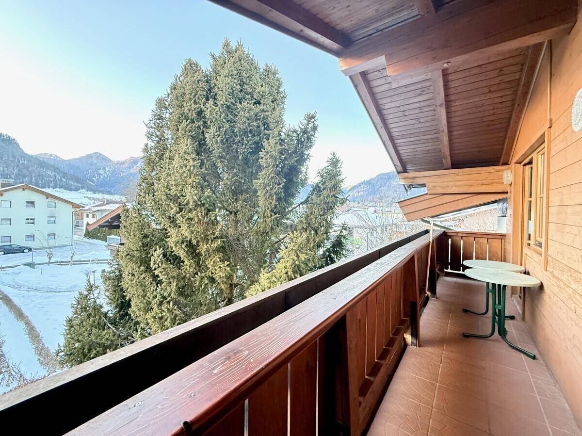 Geräumiger Holzbalkon mit Sitzgelegenheiten und Blick auf die verschneite Berglandschaft.