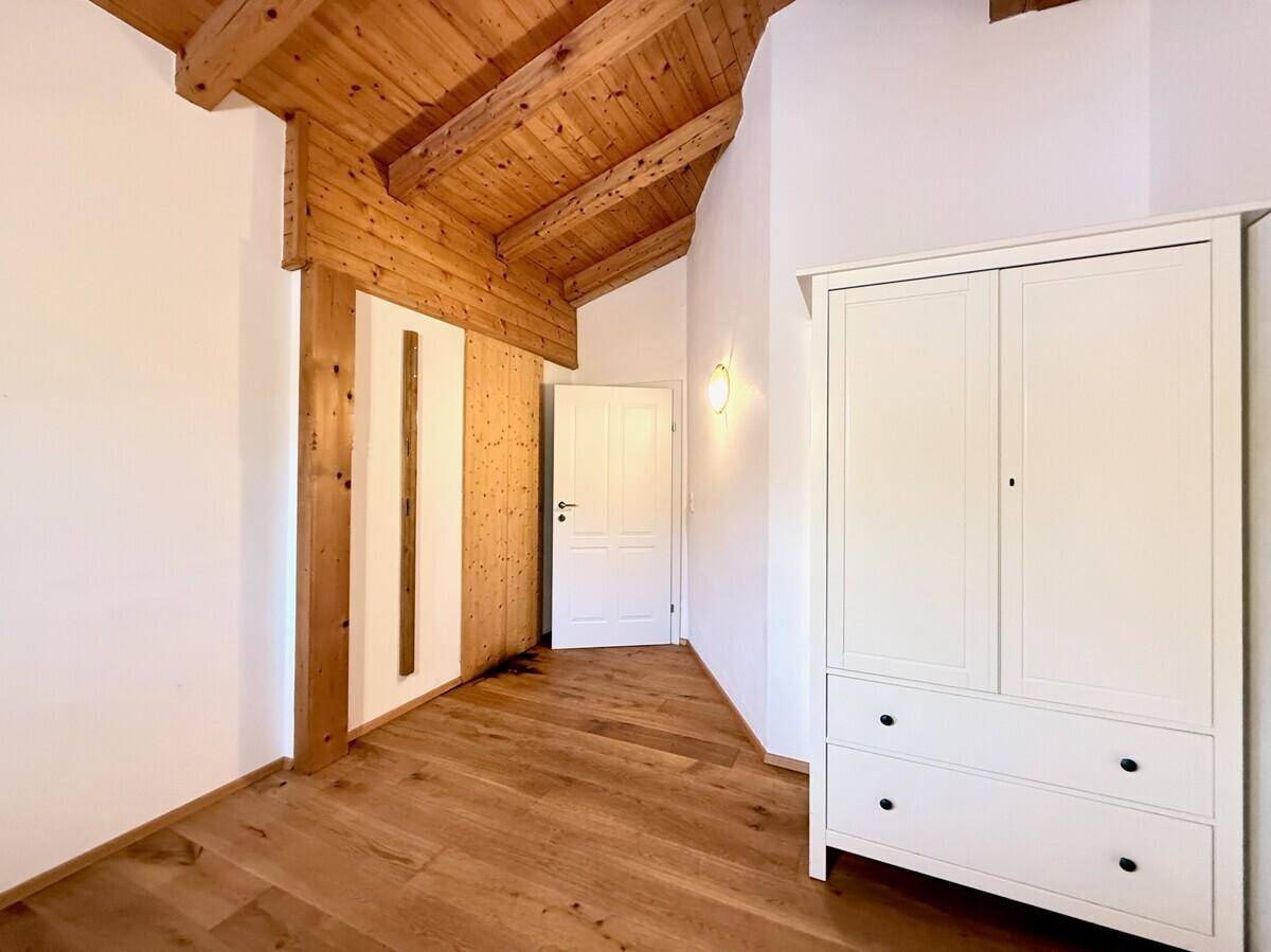 Schlafzimmer mit Holzboden, Holzbalkendecke und weißem Kleiderschrank.