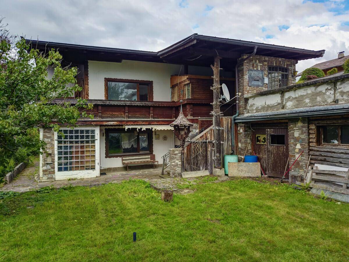 Rückseite des Hauses mit Garten, kleiner Terrasse und Nebengebäude im Grünen.