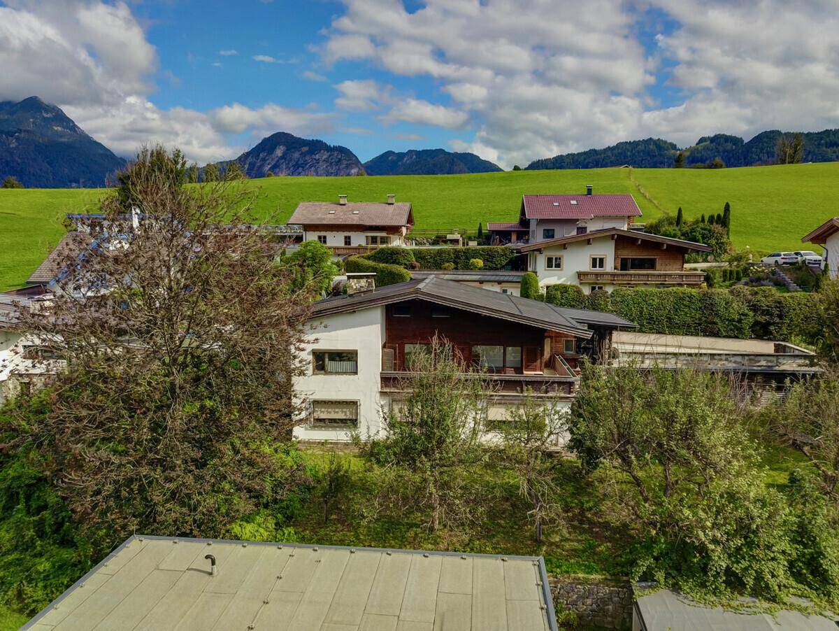 Luftaufnahme des Hauses mit Fassade, umgebendem Grün und Bergen im Hintergrund.