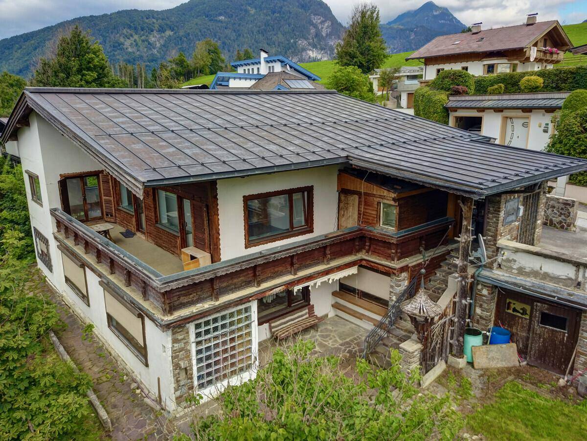 Nahaufnahme des Hauses mit Holzbalkonen und traditionellen Elementen vor Bergkulisse.