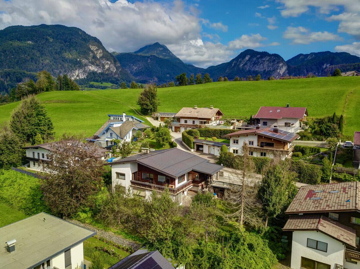 Weitläufige Luftaufnahme des Hauses in einer Siedlung mit grünen Wiesen und Bergen.