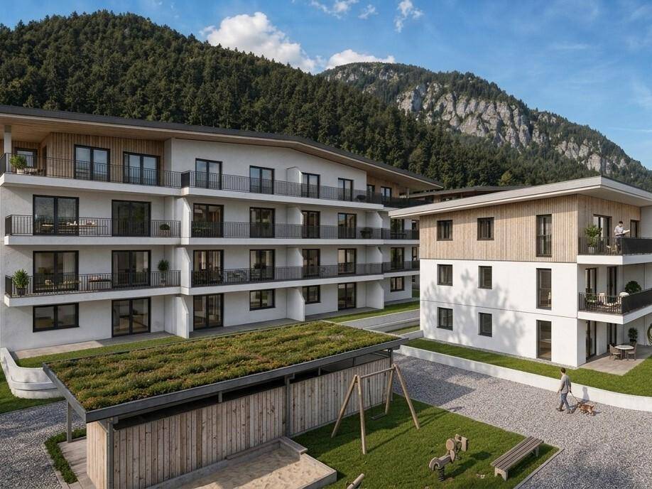 Moderne Wohnanlage mit mehreren Gebäuden, umgeben von Bergen und mit Kinderspielplatz.