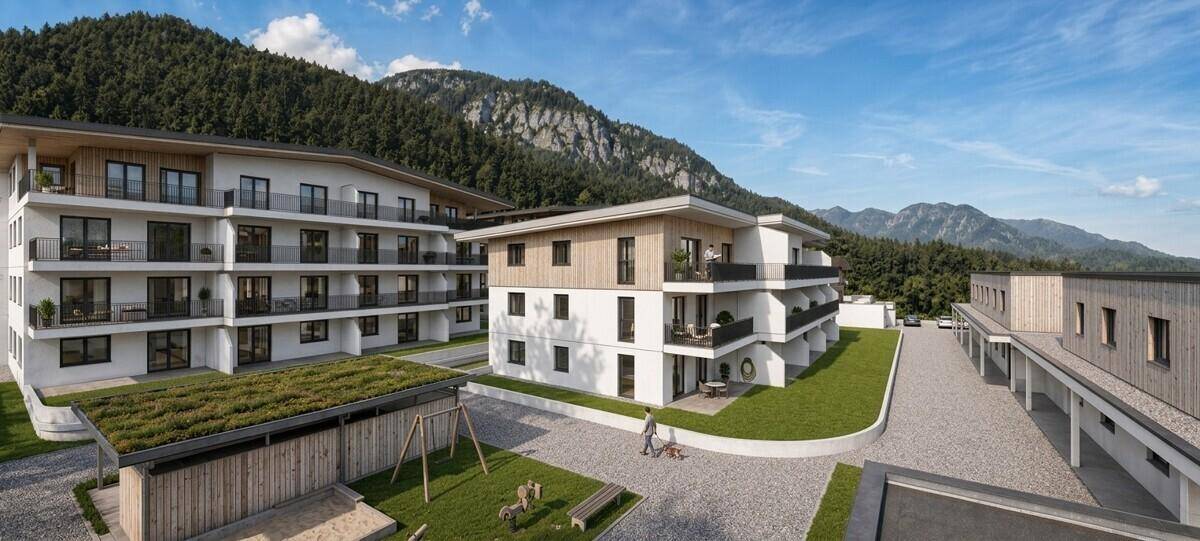 Moderne Wohnanlage mit mehreren Gebäuden, umgeben von grüner Landschaft und Bergen.