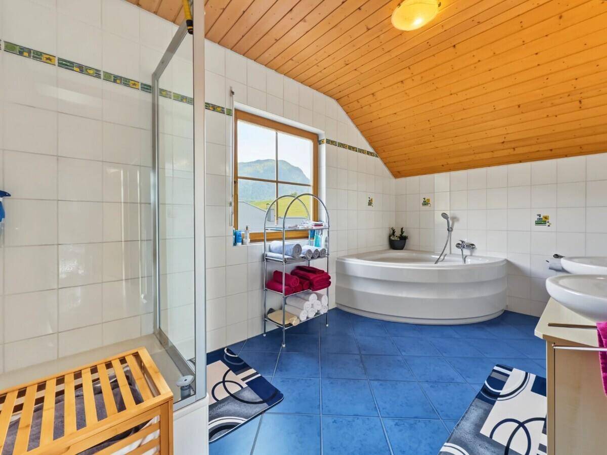 Geräumiges Badezimmer mit Eckbadewanne, Dusche, blauen Fliesen und einer Holzdecke.