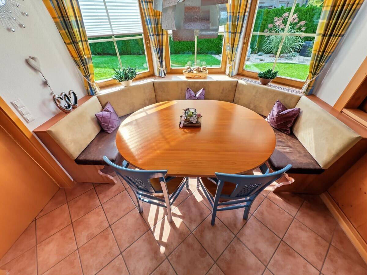 Gemütlicher Essbereich mit Eckbank, Holztisch und großen Fenstern, die den Blick in den Garten freigeben.