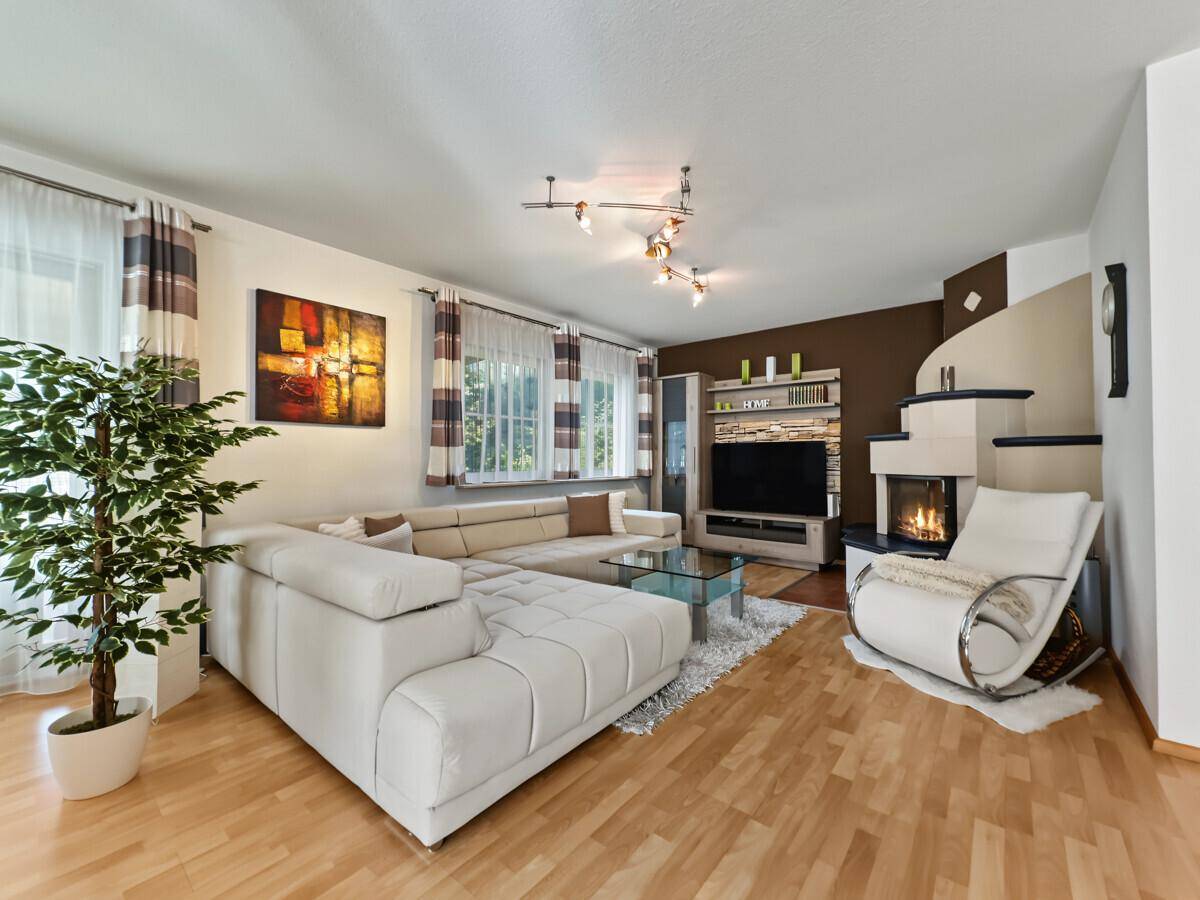 Helles Wohnzimmer mit großem Ecksofa, Holzboden und modernem Kachelofen als Blickfang.