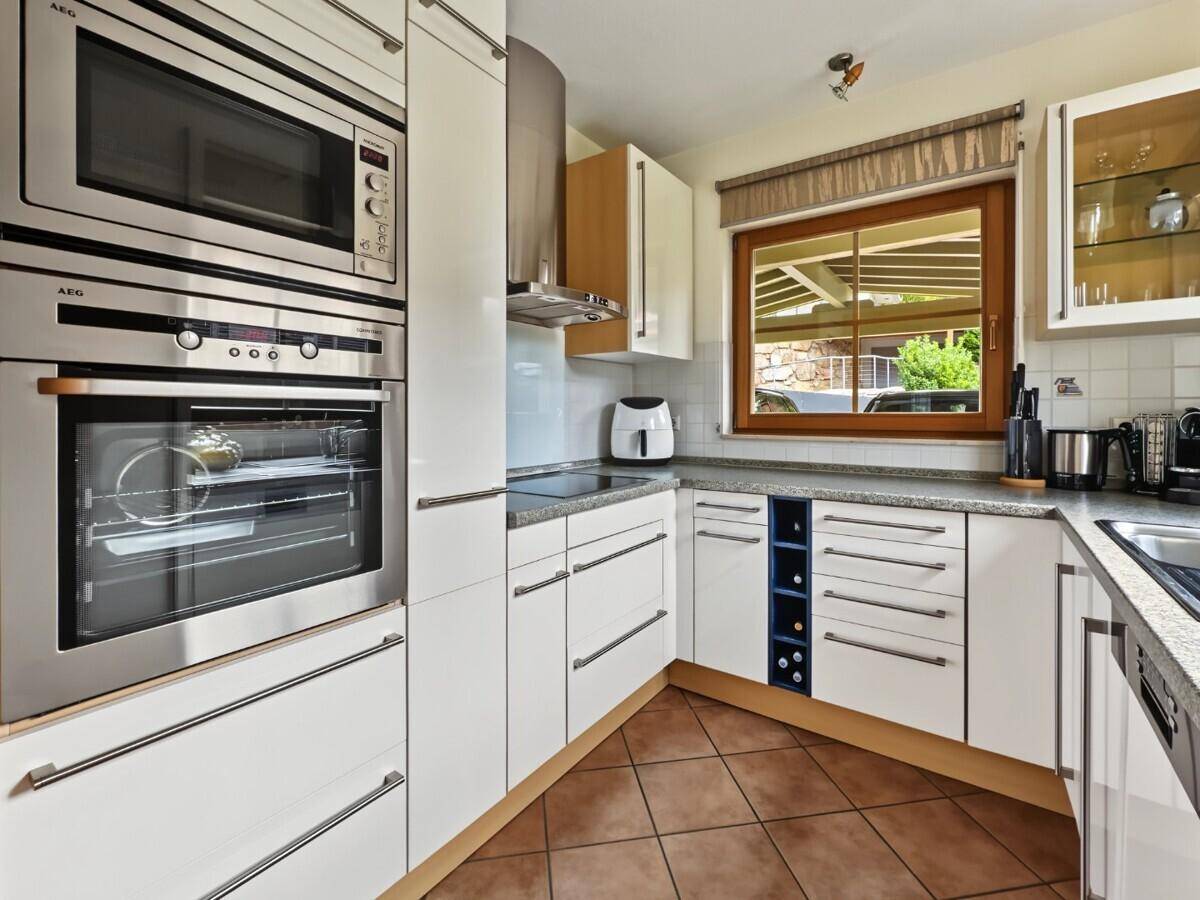 Moderne Einbauküche mit weißen Hochglanzfronten, integrierten AEG-Geräten und Fensterblick.
