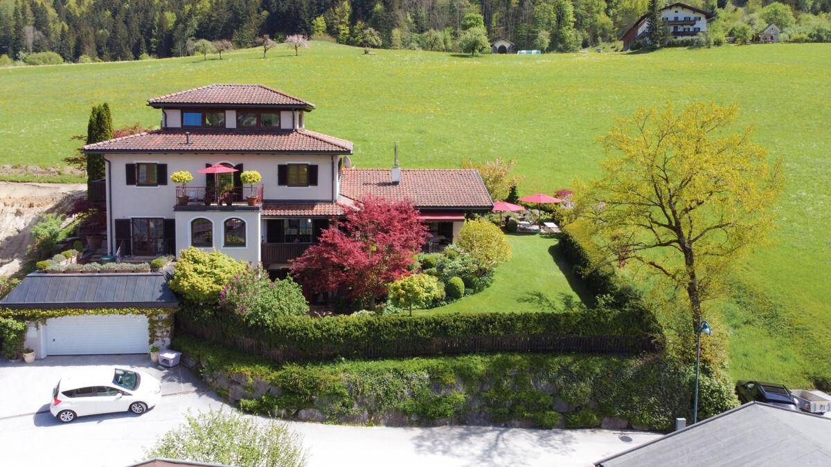 Großzügiges Anwesen mit gepflegtem Garten, Balkon und Doppelgarage, umgeben von grüner Hügellandschaft.