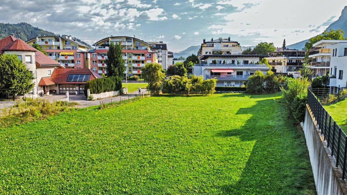 Großzügige Grünfläche umgeben von Wohngebäuden und Bergen unter einem bewölkten Himmel.