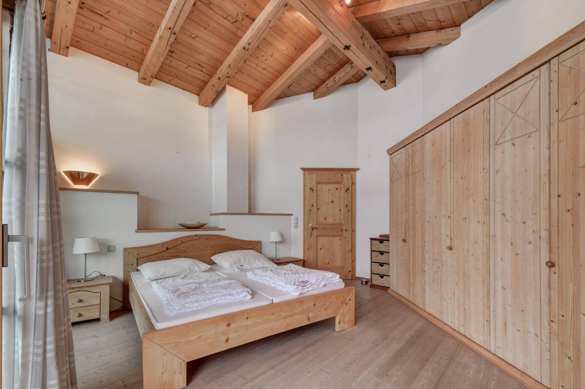 Helles Schlafzimmer mit Holzbalkendecke, Einbauschränken und Zugang zu einem Außenbereich.