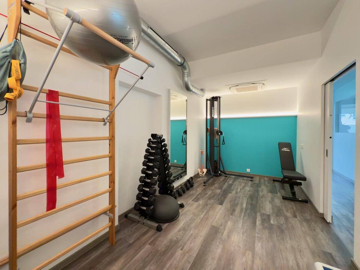 Trainingsraum mit Sprossenwand, Hanteln und weiteren Fitnessgeräten für Physiotherapie.