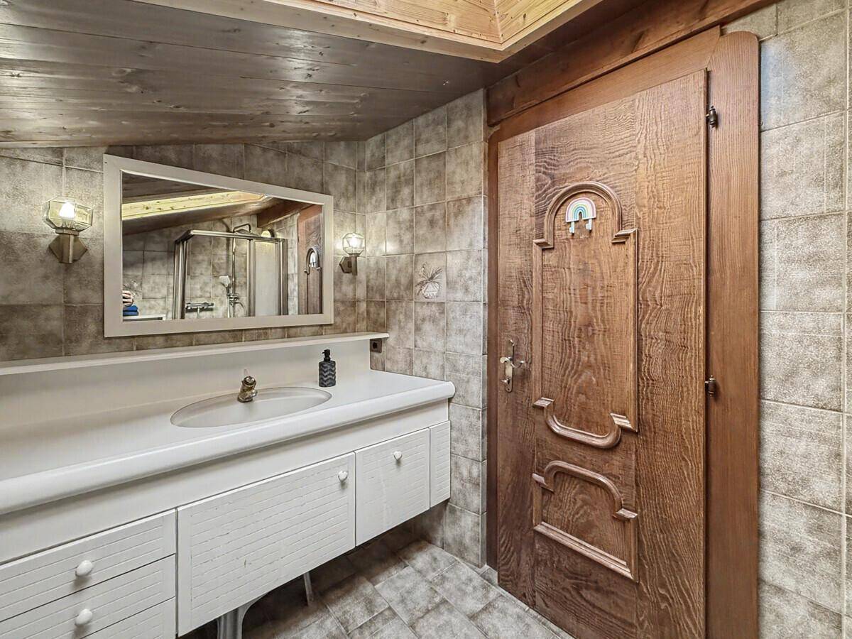 Badezimmer mit Waschtisch, Spiegel und Holztür, ergänzt durch Fliesen und Holzdecke.