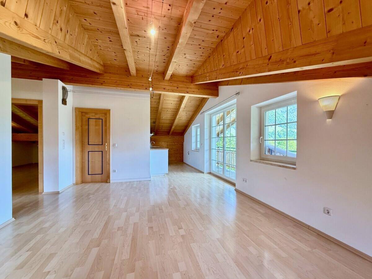Heller Wohnraum mit Holzbalkendecke, Parkettboden und Zugang zu einem Balkon.