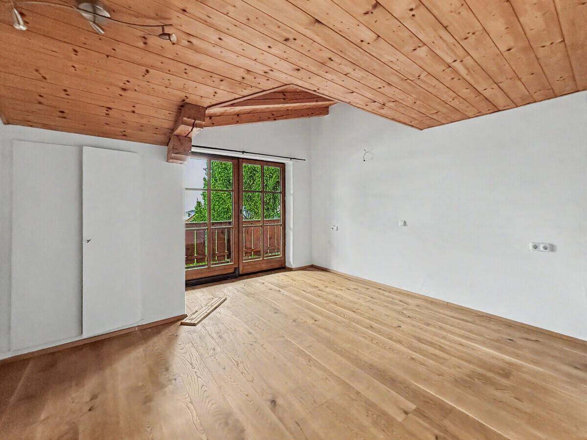 Schlafzimmer mit Holzbalkendecke, Holzboden und Zugang zu einem Balkon mit grüner Aussicht.