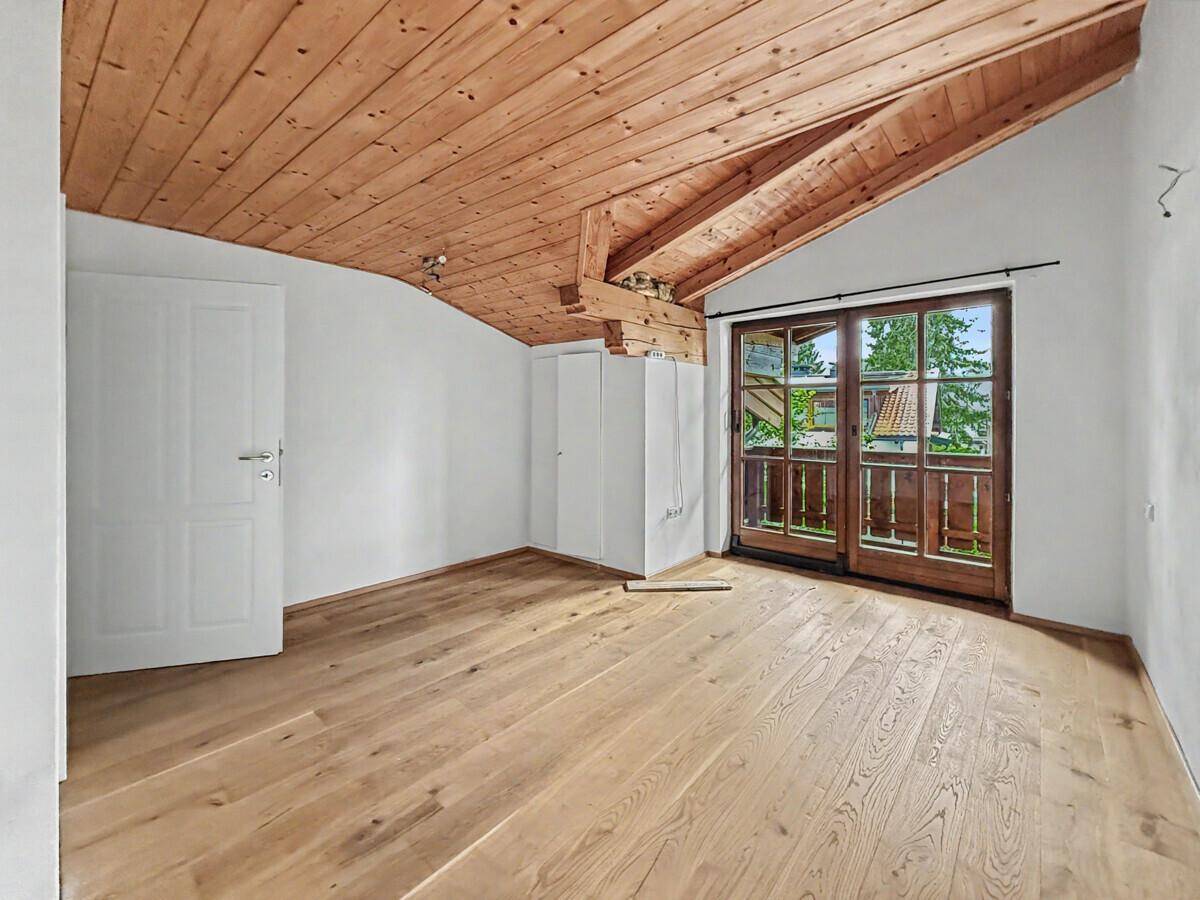 Geräumiges Schlafzimmer mit Holzbalkendecke, Holzboden und Balkonzugang.